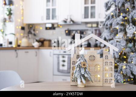 Schlüssel auf Weihnachtsbaum und winziges Haus auf gemütlichem Haus mit Weihnachtsdekor auf dem Tisch der festlichen weißen Küche. Geschenk für Neujahr. Versicherung, Wechsel zu neuer Stockfoto