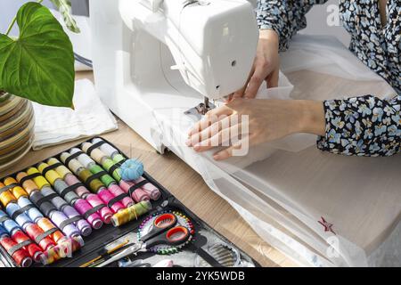 Die Hand einer Frau näht Tümpel an eine elektrische Nähmaschine. Füllung des Fadens in die Nähnadel, Einstellung der Spannung. Komfort im Haus, a h Stockfoto