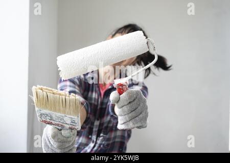 Verwirrte Frau in Malerwalze und weißer Farbe für Wände in Händen Nahporträt. Bauarbeiten und kosmetische Reparaturen im Haus, Wandmalerei, ti Stockfoto