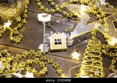 Hausschlüssel mit Schlüsselanhänger Hütte auf einem festlichen Hintergrund mit Pailletten, Sterne, Lichter von Girlanden. Frohes neues Jahr-Holzbriefe, Grüße, Gruß ca. Stockfoto