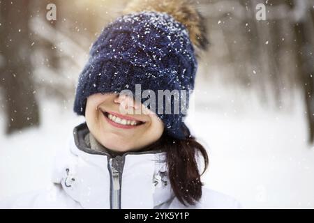 Eine Frau mit einem warmen Strickhut über die Augen gezogen lächelt und genießt den Schnee, die Frühlingssonne. Outdoor-Aktivitäten, Saisonalität, Winter, Schnee schmilzt. Stockfoto