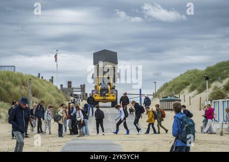 Eine Menschenmenge beobachtet, wie ein Traktor mit Strandkabine am Ende der Saison auf Texel auf einer Sandstraße fährt Stockfoto