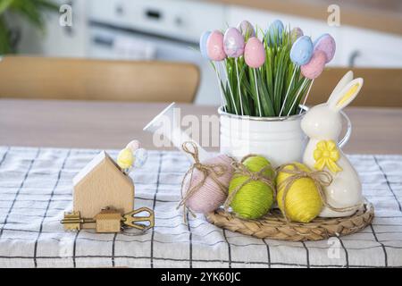 Schlüssel und winziges Haus mit gemütlichem Haus mit Osterdekor mit Kaninchen und Eiern auf dem Tisch der Küche. Bau, Entwurf, Projekt, Umzug in ein neues Haus, Hypothek, Stockfoto