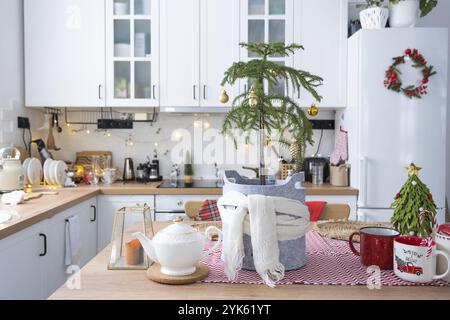 Festliche Weihnachtsdekor in weißer Küche, festliches Frühstück, weiße scandi-Innenausstattung. Araukarien als Weihnachtsbaum sind dekoriert und in einen Schal eingewickelt Stockfoto