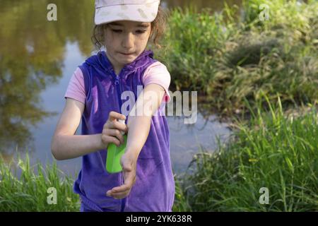 Mädchen sprüht Mückenspray auf die Haut in der Natur, die ihre Hände und Füße beißen. Schutz vor Insektenstichen, abweisend sicher für Kinder. Außenrekr Stockfoto