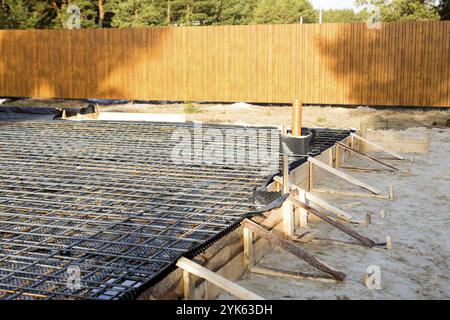 Eisenbeschläge auf einer Holzschalung mit verlegten Rohren sind die Grundlage für das Ausgießen des Fundaments des Hauses mit einer Betonplatte. Bau der Hütte Stockfoto