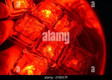 Schöne und leuchtend rot leuchtende Eiswürfel schweben in einer Edelstahlschöpfel mit klarem Wasser. Plastikgegenstände in Form von Eiswürfeln. Stockfoto