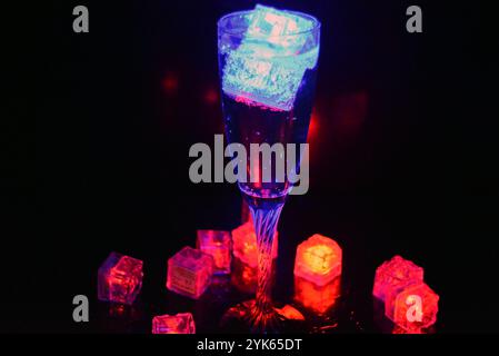 Wunderschöner und leuchtend blauer Eiswürfel schwimmt in einem Glas Sektglas mit einem Getränk. Plastikgegenstände in Form von Eiswürfeln. Stockfoto