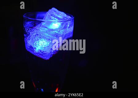 Wunderschöner und leuchtend blauer Eiswürfel schwimmt in einem Glas Sektglas mit einem Getränk. Plastikgegenstände in Form von Eiswürfeln. Stockfoto