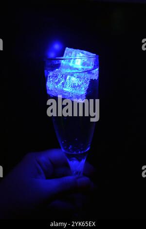 Wunderschöner und leuchtend blauer Eiswürfel schwimmt in einem Glas Sektglas mit einem Getränk. Plastikgegenstände in Form von Eiswürfeln. Stockfoto
