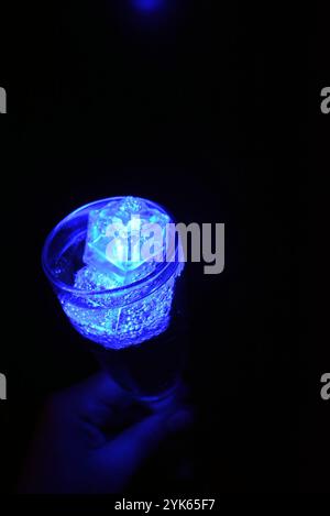 Wunderschöner und leuchtend blauer Eiswürfel schwimmt in einem Glas Sektglas mit einem Getränk. Plastikgegenstände in Form von Eiswürfeln. Stockfoto