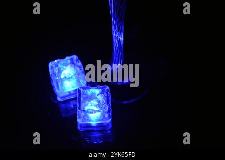 Wunderschöner und leuchtend blauer Eiswürfel schwimmt in einem Glas Sektglas mit einem Getränk. Plastikgegenstände in Form von Eiswürfeln. Stockfoto