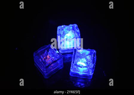 Wunderschöner und leuchtend blauer Eiswürfel schwimmt in einem Glas Sektglas mit einem Getränk. Plastikgegenstände in Form von Eiswürfeln. Stockfoto