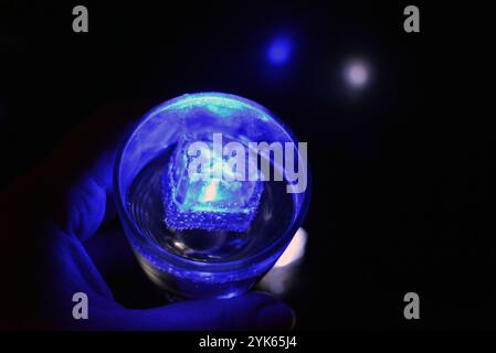 Wunderschöner und leuchtend blauer Eiswürfel schwimmt in einem Glas Sektglas mit einem Getränk. Plastikgegenstände in Form von Eiswürfeln. Stockfoto