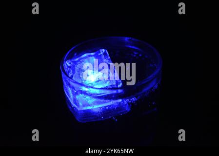 Wunderschöner und leuchtend blauer Eiswürfel schwimmt in einem Glas Sektglas mit einem Getränk. Plastikgegenstände in Form von Eiswürfeln. Stockfoto