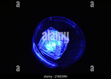 Wunderschöner und leuchtend blauer Eiswürfel schwimmt in einem Glas Sektglas mit einem Getränk. Plastikgegenstände in Form von Eiswürfeln. Stockfoto