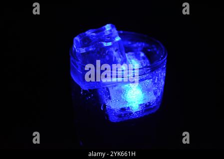 Wunderschöner und leuchtend blauer Eiswürfel schwimmt in einem Glas Sektglas mit einem Getränk. Plastikgegenstände in Form von Eiswürfeln. Stockfoto