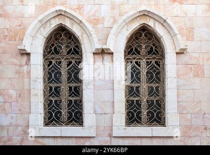Ein wunderschön gefertigtes gotisches Fenster ziert eine alte Steinmauer mit künstlerischen Metallarbeiten. Stockfoto