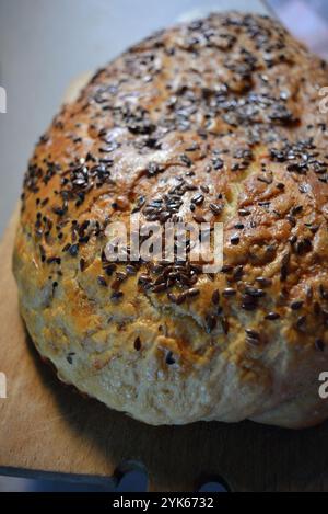 Frisches, köstliches geröstetes Brot, das zu Hause zubereitet wird. Ein Brotlaib mit schwarzen Sesamsamen sitzt auf weißem Pergamentpapier. Stockfoto