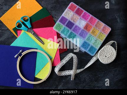 Buntes Bild von Bastelbedarf. Filzstoff, Glasperlen, Stickreif, Schere und Profil auf dunklem Hintergrund. Hobby- und Freizeitkonzept. Stockfoto