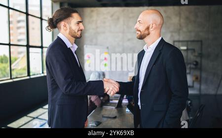 Zwei Männer in Anzügen begrüßen einander mit einem Handschlag in einem modernen Büro Stockfoto