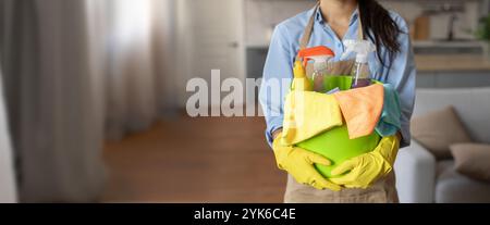 Eine Person hält beim Aufräumen in Innenräumen Reinigungsmaterial in einem grünen Korb Stockfoto