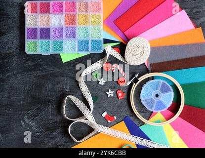 Buntes Bild von Bastelbedarf. Filzstoff, Glasperlen, Stickreif, Schere und Profil auf dunklem Hintergrund. Hobby- und Freizeitkonzept. Stockfoto