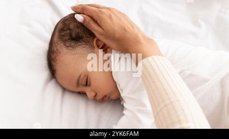 Schwarze Mutter streichelt mit der Hand und schläft den Kopf des Babys im Bett, abgeschnitten Stockfoto