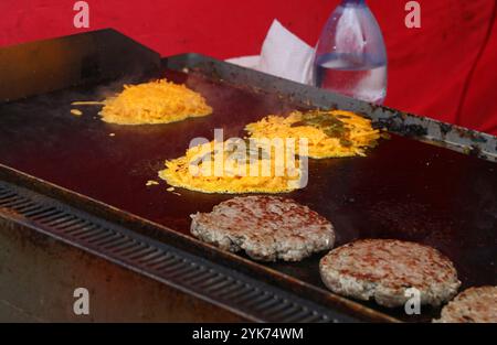 Gemahlene Rindfleischpastete und geriebener Käse mit Jalapenos brutzeln auf einem großen, flachen Grill, was die Zubereitung von Käseeburgern in einem schnellen F Stockfoto