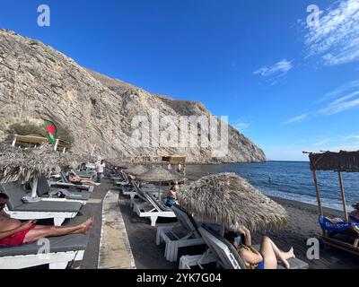 Santorini, Südägäis – GR – 20. Oktober 2024 Perissa Beach in Santorini, Griechenland, bietet eine entspannte Atmosphäre mit Sonnenanbetern auf Liegestühlen unter dem Dach Stockfoto