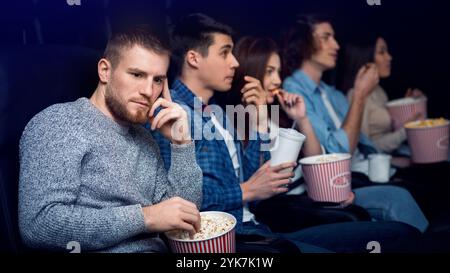 Dumpfer Film. Gelangweilter Mann mit Gesellschaft von Menschen im Kino Stockfoto