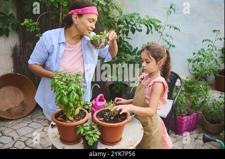 Mutter und Tochter arbeiten gerne gemeinsam im Garten und pflegen Topfpflanzen auf einer Terrasse. Sie teilen einen Moment des Lernens und der Bindung, umgeben von der Natur. Stockfoto