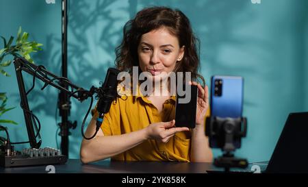 Smartphone im Halter, das Aufnahmen von Rezensenten aufnimmt, die mit Zuschauern über das neu veröffentlichte Mobiltelefon diskutieren. Influencer chatten mit Fans während des Streams, filmt die neueste Generation der Telefonberichte, Kamera A Stockfoto