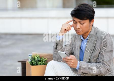 Ein Mann im Anzug sitzt draußen und schaut auf sein Handy Stockfoto