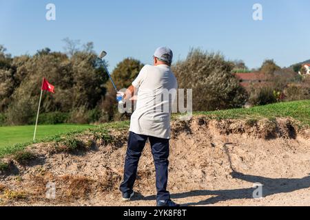 Ältere Golfer sind konzentriert, während er den Ball aus einem Sandbunker meisterhaft schlägt und versucht, ihn während eines Golfspiels auf dem Grün zu platzieren. Sein Können und seine Präzision Stockfoto