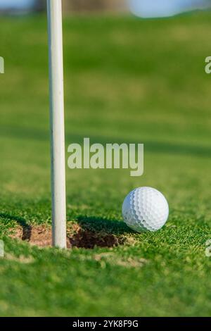Detaillierte Nahaufnahme eines Golfballs, der am Rand des Lochs auf einem makellosen Grün thront und die Spannung und Präzision des Augenblicks in einem ruhigen G festlegt Stockfoto