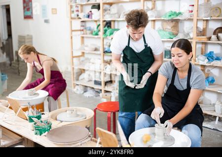 Töpferin unterrichtet junge Lehrlinge in der Werkstatt, wie man Töpferei auf Töpferrad macht Stockfoto