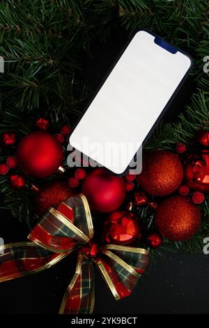 Handy-Mock-up-Vorlage weißen Bildschirm auf handgemachten Weihnachtskranz. Festliche Stimmung Neujahrsfeier. Postkartendekoration, Draufsicht, flach gelegen Stockfoto