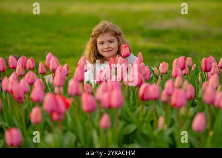 Spannfeder. Kinderspiel im Freien in einem schönen Frühlingsgarten. Kindergesicht in Tulpenblüten. Entzückendes kleines Kind im blühenden Tulpengarten auf der wunderschönen Stockfoto