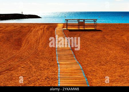 Hölzerner Pfad führt zum Meer an einem Sandstrand. Die Leitung wird von blauen Linien begrenzt und erstreckt sich vom Vordergrund bis zur Mitte. Im Hinterland Stockfoto