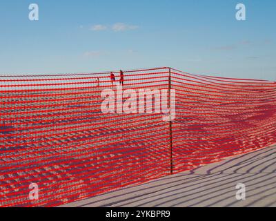 Weiter Blick über den Gehweg durch den orangefarbenen Sicherheitszaun für 3 Personen am Sandstrand in Richtung Golf von Mexiko. Reifenspuren im Sanddünen-Strand. Stockfoto