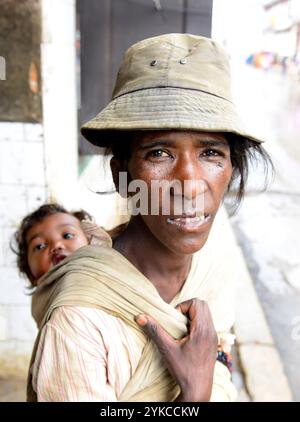 Porträt einer madagassischen Frau mit ihrem Baby an den Rücken gefesselt. Foto gemacht in Antsirabe, Madagaskar. Stockfoto