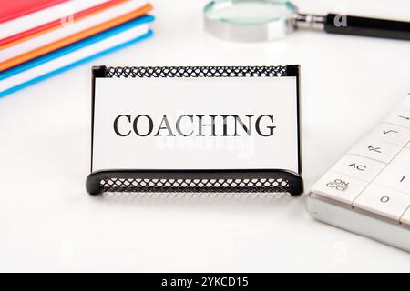 Geschäftskonzept. Der Satz, Text, Wortwahl COACHING ist auf einer Visitenkarte in einem Ständer auf weißem Hintergrund geschrieben. Stockfoto