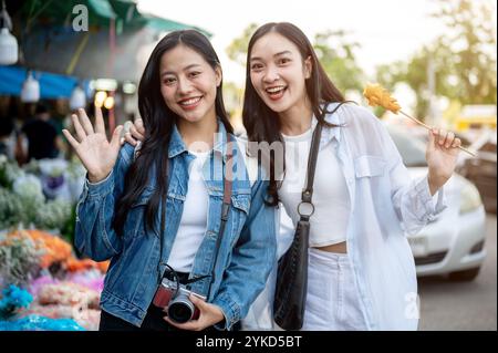 Ein Porträt von zwei fröhlichen und schönen asiatischen Frauen schlendern durch einen Blumenmarkt in Thailand, lächelnd und winkend in die Kamera. Reise, Urlaub, Urlaub Stockfoto