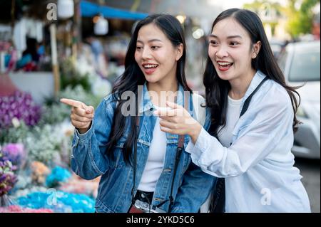 Zwei fröhliche asiatische Frauen genießen es, Blumen auf einem Blumenmarkt gemeinsam auszuwählen und zu kaufen, während sie durch Thailand reisen. Urlaub, Reise, Lebensstil Stockfoto