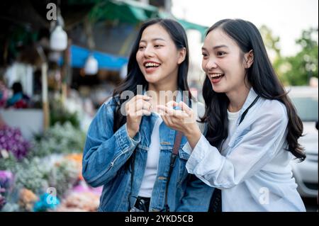 Zwei fröhliche asiatische Frauen genießen es, Blumen auf einem Blumenmarkt gemeinsam auszuwählen und zu kaufen, während sie durch Thailand reisen. Urlaub, Reise, Lebensstil Stockfoto