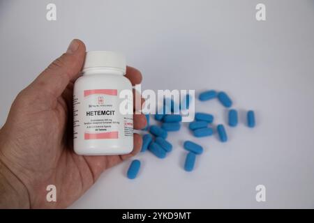 Flasche Hetemcit-Präexpositionsprophylaxe in einer kaukasischen Hand. Im Hintergrund sind blaue Pillen unscharf vor weißem Hintergrund. Stockfoto