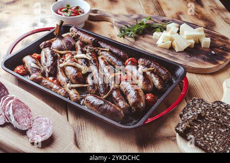 Grillpfanne mit leckeren hausgemachten Hühnchen-, Rind- und Schweinefleisch-Würstchen, Pilzen und Tomaten auf einem Holztisch mit Ketchup, Brot und Käse. Hoch Stockfoto