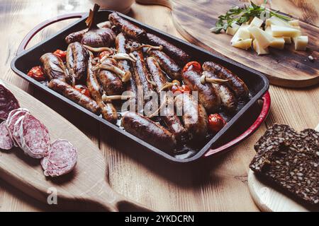 Grillpfanne mit leckeren hausgemachten Hühnchen-, Rind- und Schweinefleisch-Würstchen, Pilzen und Tomaten auf einem Holztisch mit Ketchup, Brot und Käse. Hoch Stockfoto