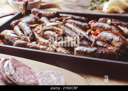 Grillpfanne mit leckeren hausgemachten Hühnchen-, Rind- und Schweinefleisch-Würstchen, Pilzen und Tomaten auf einem Holztisch mit Ketchup, Brot und Käse. Hoch Stockfoto